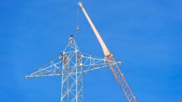 Construction crews and crane working on a high-voltage electricity transmission tower