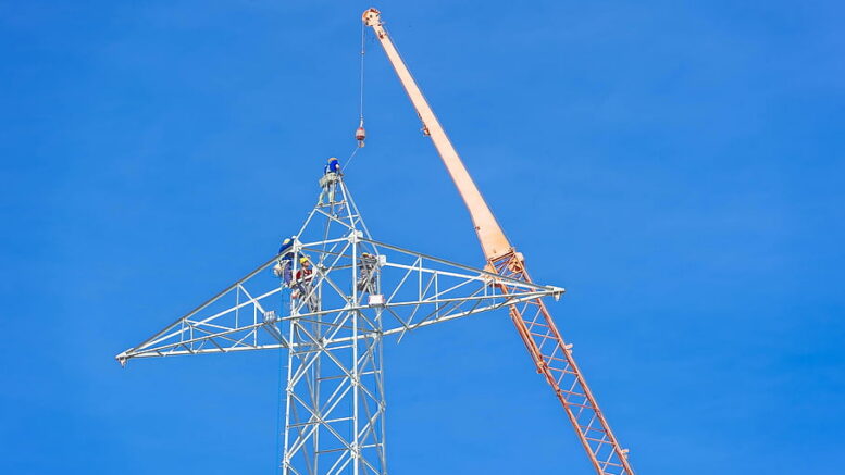 Construction crews and crane working on a high-voltage electricity transmission tower